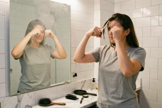Femme se coupant les pointes seule devant un miroir de salle de bain avec des ciseaux de coiffure