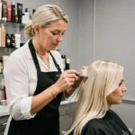 Coiffeuse professionnelle appliquant une patine neutralisante sur cheveux blonds en salon