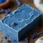 Savon Nila bleu fait maison posé sur une surface en bois avec de la poudre d'indigo et du beurre de karité brut